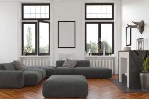 Cozy living room interior with fireplace and radiators below tall windows overlooking the garden and a comfortable grey upholstered lounge suite with blank picture frame on the wall. 3d Rendering.